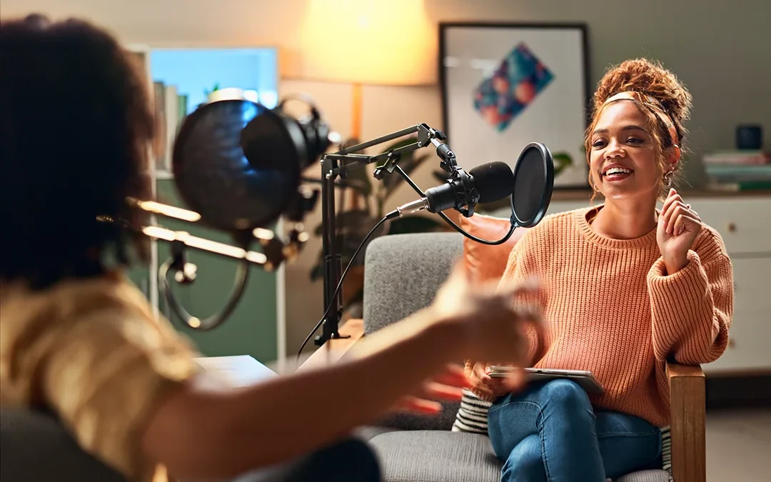 Two people recording a podcast conversation using microphones in a relaxed indoor setting