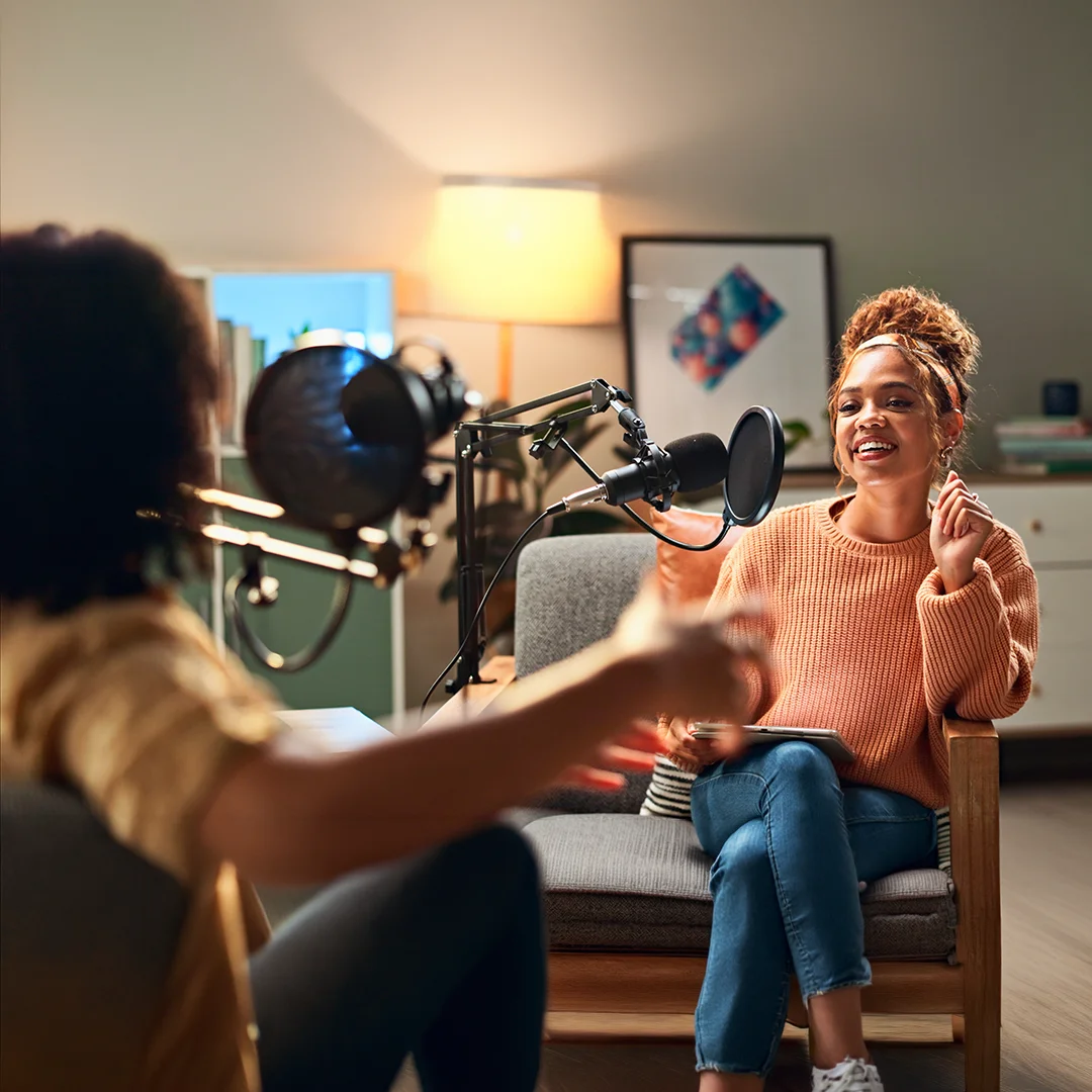 Two people recording a podcast conversation using microphones in a relaxed indoor setting